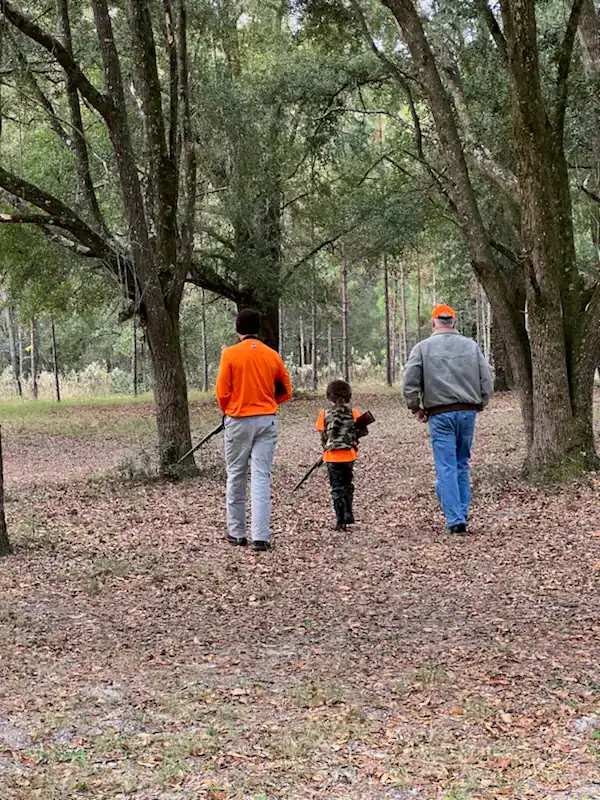 Two adults and a child hunting in a wooded forest